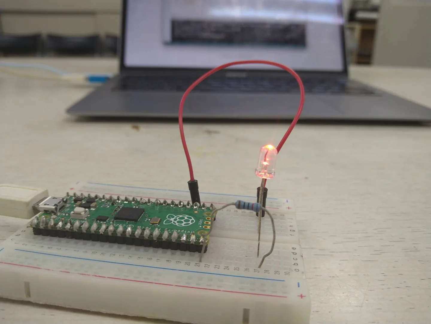 ブレッドボードに載せたRaspberry Pi Picoと、赤く点灯したLED・抵抗・ジャンパー線