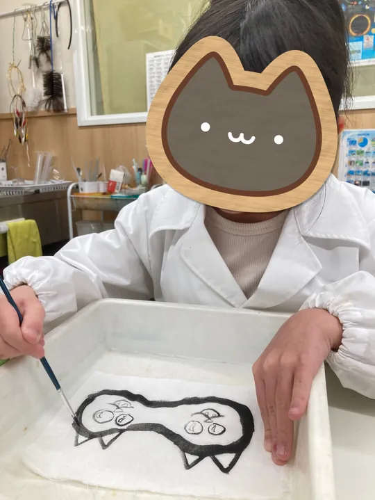 小学3年生が白い布に炭水で絵を描いているところ